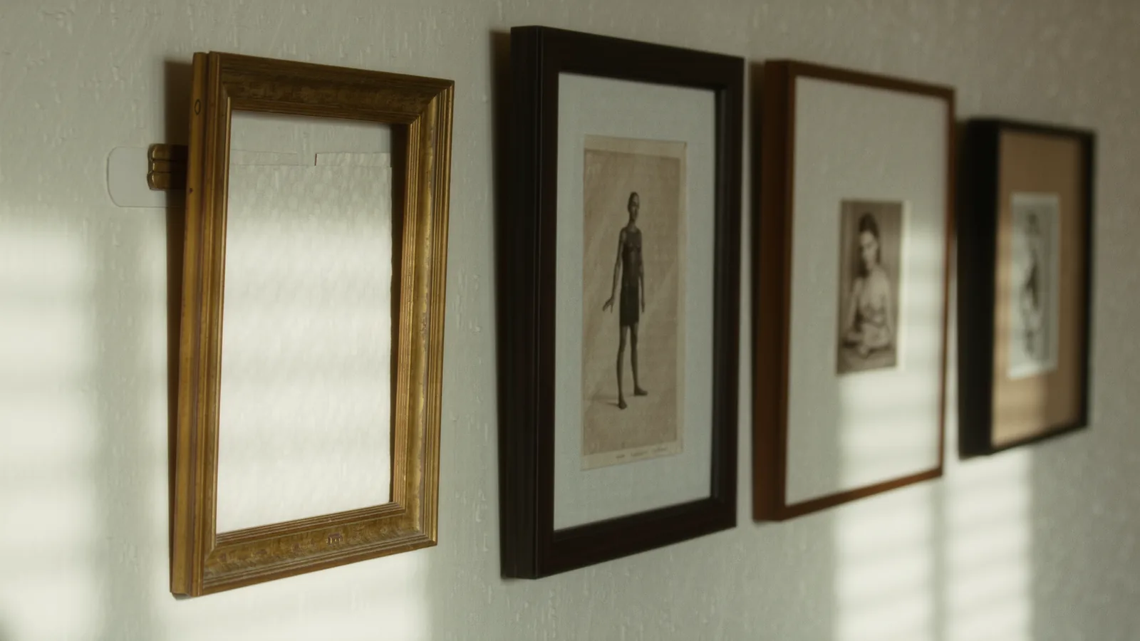 An empty brass picture frame on an ivory wall beside filled frames